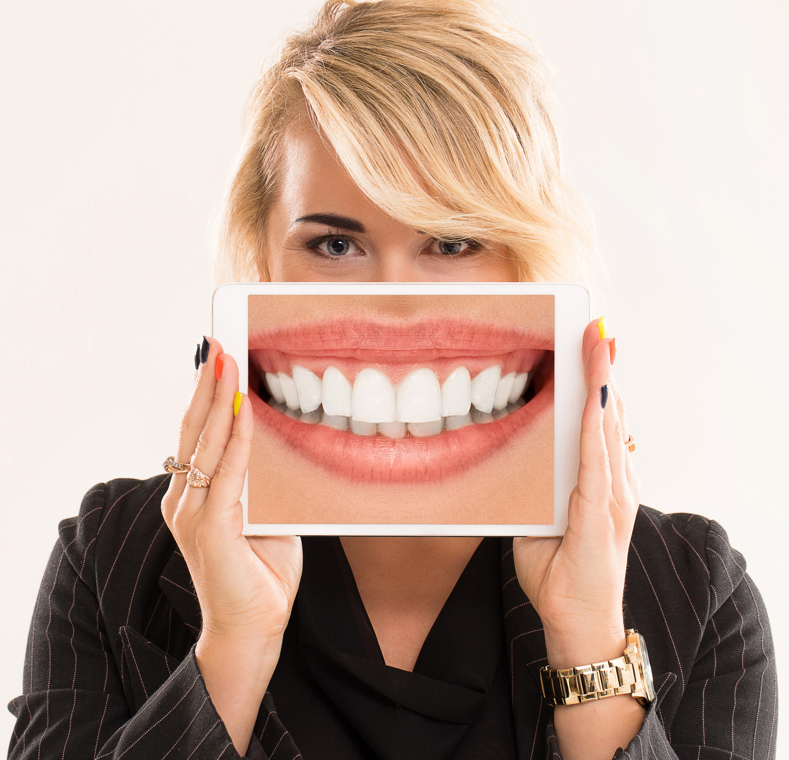 Beautiful woman with blonde hair and black suit is holding a tablet with large teeth on a screen